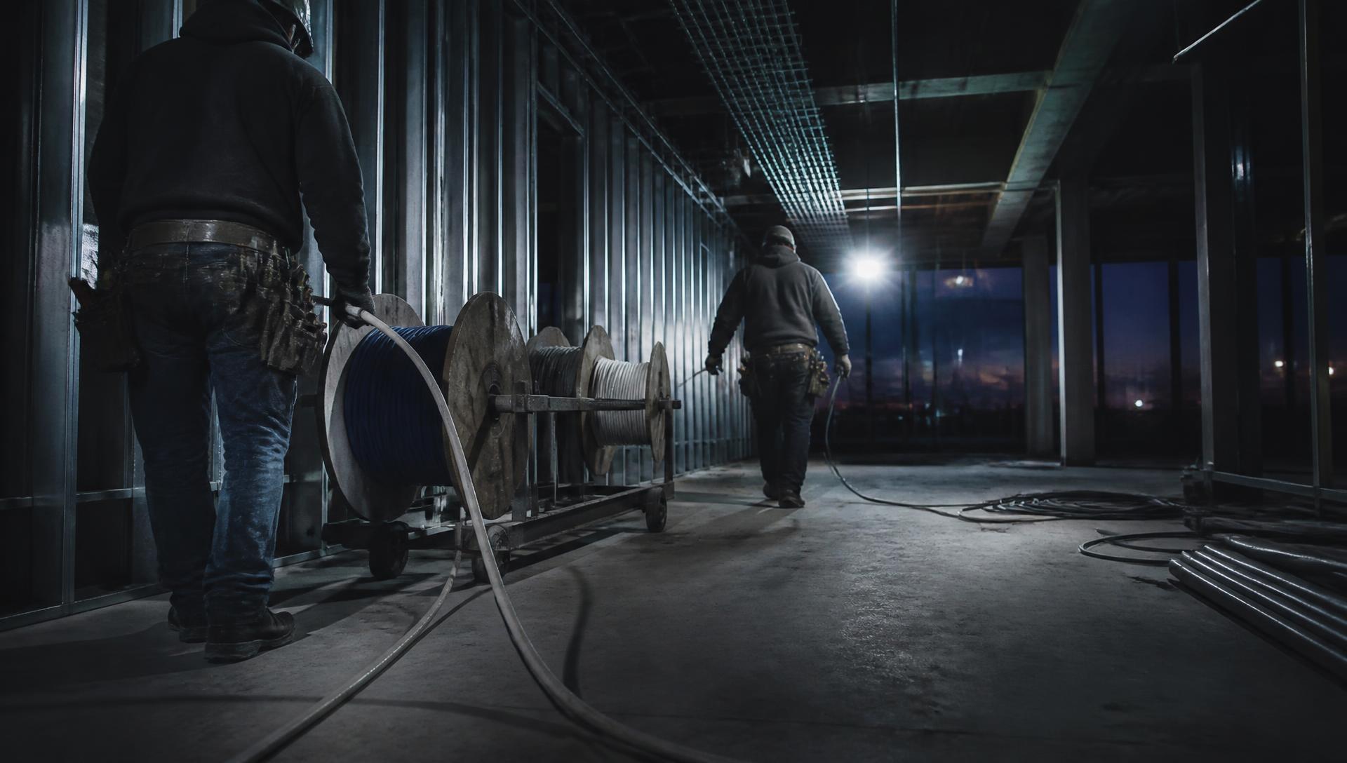 Technicians pulling cable on a commercial jobsite at dusk